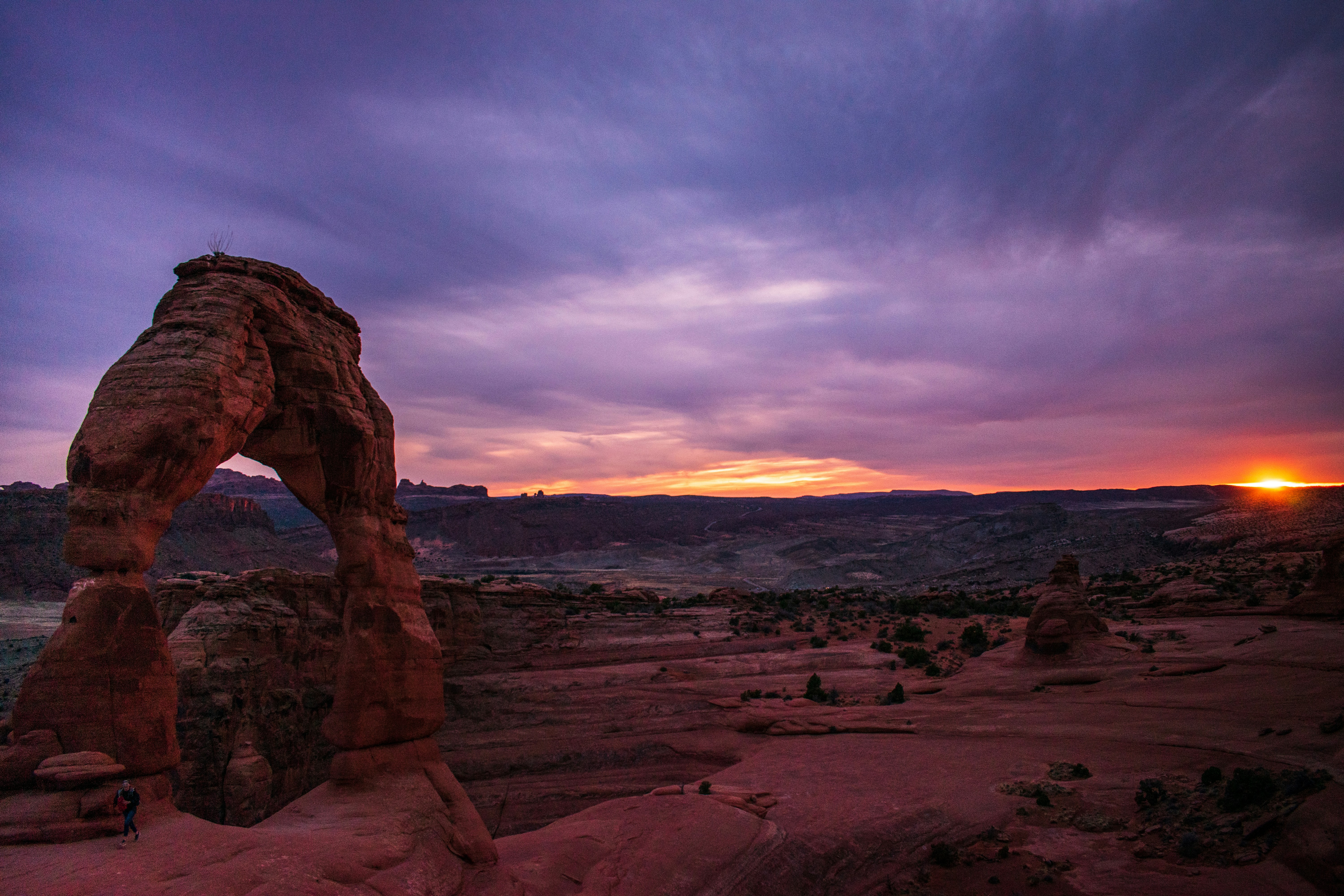 Photo of an arch rock formation in the background with a sunset